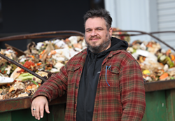 Robert Putney, Impact Earth founder and CEO, in front of a Dumpster filled with food waste. - PHOTO BY MAX SCHULTE