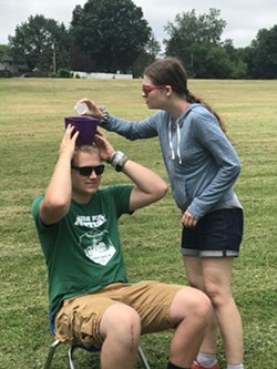 A camper pours water into a bucket on top of a counselor's head in a camp activity in the summer of 2019. - PHOTO BY EMMA BENZ