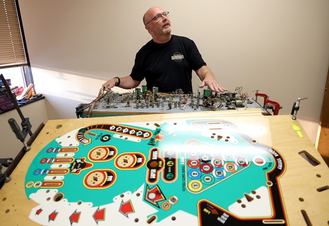 Bruce Nightingale explains the intricacies of a "playfield swap" being done on a 1977 Eight Ball game, in which all the circuitry is transferred from an old playfield to a new one. - PHOTO BY MAX SCHULTE