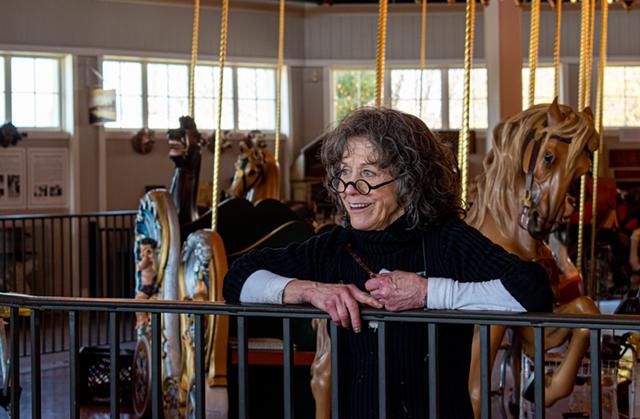 A woman smiles, leaning against the bars around a carousel.
