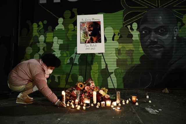 A vigil-goer leaves a candle beneath a portrait of Memphis's Tyre Nichols.