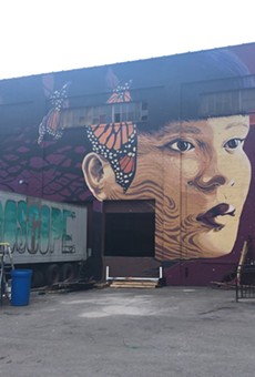 Jess X Snow's finished mural for WALL\THERAPY 2017, on the lot-facing wall at 936 Exchange Street. On the truck is an in-progress piece by Cruk FUA.